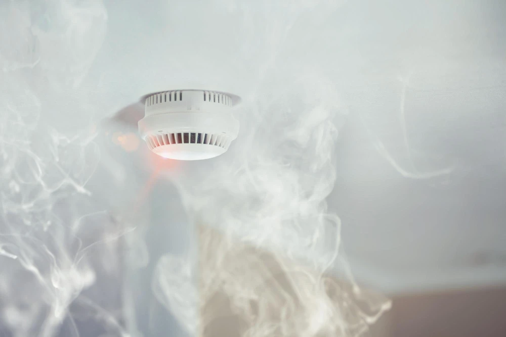 Smoke alarm on ceiling with smoke rising up towards it